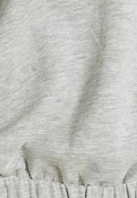 Tessuto di cotone grigio chiaro con una morbida texture, dotato di un elastico arricciato in vita e dettagli di cucitura visibili.