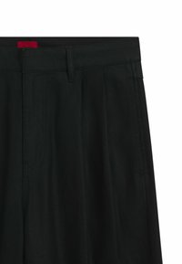Black trousers with a smooth texture, featuring pleats, a straight cut, and a red brand tag on the waistband. Minimalist design.