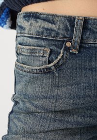 Faded blue denim jeans with a high waist, silver button, and a small back pocket featuring frayed edges and distinct stitching.