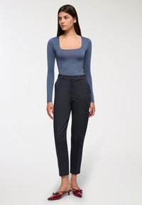 Dopasowany bodysuit z długim rękawem w kolorze niebieskim, czarne spodnie z wysokim stanem oraz czerwone mule na obcasie z detalem w postaci kokardy, na neutralnym tle.