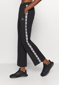 Černé sportovní kalhoty s elastickým pasem, zdobené bílými bočními pruhy s malými logy. Kombinov�ány s černými teniskami.