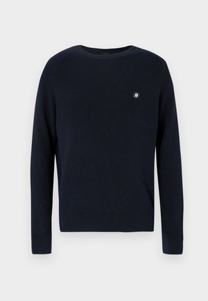 Tumši zils adīts džemperis arapaļas formas kakla izgriezumu, ribota tekstūra, garām piedurknēm un nelielu logotipu kreisā krūtīs.