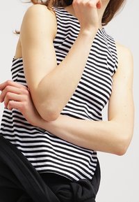 Top sin mangas a rayas en blanco y negro con cuello redondo, hecho de una tela suave, que presenta un diseño ajustado y una apariencia texturizada.