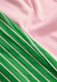 Ribbet rosa stof og glat grønt stof med hvide striber arrangeret diagonalt. Den grønne sektion har kontrasterende lodrette striber.