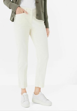 Cream-colored corduroy pants with a slim fit, featuring front pockets and a button closure, paired with white sneakers.