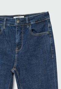 Ciemnoniebieskie dżinsy z denimu o standardowym fasonie z pięcioma kieszeniami, widocznym przeszyciem w kolorze złotobrązowym oraz zapinane na guzik w pasie.