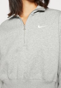 Grå zip-up sweatshirt med fleece-textur, med hög krage och en liten vit Nike-logga på vänster bröst.