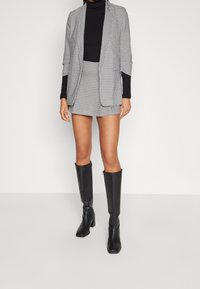 Blazer houndstooth hitam-putih dipadukan dengan rok mini yang matching, dilengkapi dengan turtleneck hitam dan sepatu bot tinggi lutut hitam.