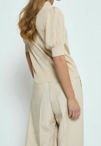 Maglione beige testurizzato con maniche a sbuffo e polsini a coste, abbinato a pantaloni beige chiaro a gamba larga con tasche laterali e pieghe.