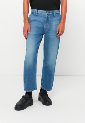 Ljusblå denimjeans med rakt ben, synlig sömnad och en något blekt finish. Bärs med svarta avslappnade skor.