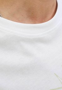Camiseta de algodón blanca con cuello redondo, que presenta una textura suave y un diseño de impresión sutil en verde claro.
