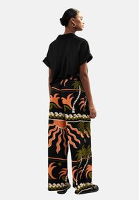 Camisa negra de manga corta combinada con pantalones de pierna ancha que presentan atrevidos patrones tropicales en naranja y verde sobre un fondo negro.