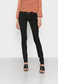 Jeans skinny pretos com uma textura suave e elástica e um design clássico de cinco bolsos, combinados com sandálias pretas de abertura. 