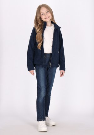 Marineblå fleecejakke med høj krave, lynlåslukning og sidelommer, parret med blå denim jeans og hvide sneakers. Glat tekstur hele vejen igennem.