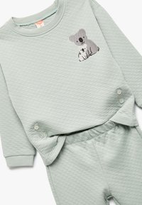 Lys grøn quiltet babyoutfit med lange ærmer, knapdetaljer og broderede grå og hvide koalaer på brystet.
