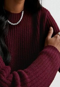 Maglione bordeaux a coste con maniche lunghe, realizzato in tessuto testurizzato. Una collana in catena argentata aggiunge un tocco metallico.