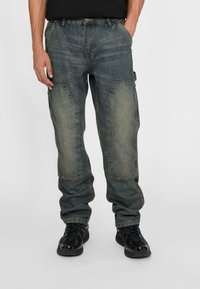 Blue denim cargo pants with light-colored knee patches, loose fit, and pockets on the sides, paired with black sneakers.