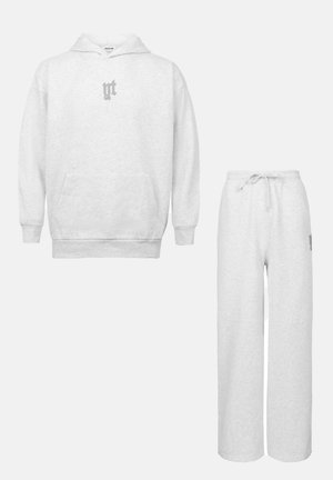 Felpa grigia con tasca frontale e un piccolo logo sul petto, abbinata a pantaloni della tuta a gamba larga con coulisse regolabile.