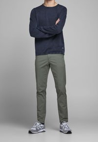 Chemise à manches longues bleu marine avec un col rond, assortie à un pantalon slim vert olive clair et des chaussures de sport grises avec des accents blancs.
