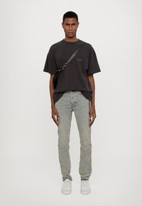 Czarna oversize'owa koszulka, jasnoniebieskie jeansy o wyblakłym kolorze z haftem po boku, białe sneakersy oraz czarna torebka na ramię z metalowymi akcentami.