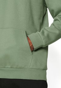 Sweatshirt en coton vert avec une poche kangourou, des poignets et un ourlet côtelés. Texture lisse avec une coupe décontractée.