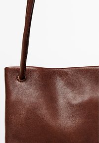 Borsa a spalla in pelle marrone con texture liscia, ampia apertura e sottile tracolla. Presenta un design minimalista senza hardware o rifiniture.
