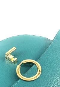 Türkisfarbene Lederhandtasche mit glatter Textur. Verfügt über goldene Beschläge, einschließlich eines kreisförmigen Akzents und eines geometrischen Logos.