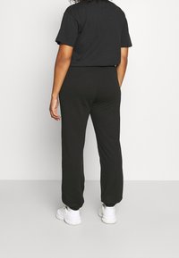 Schwarzes T-Shirt mit kurzen Ärmeln und schwarze Jogginghosen aus weichem Stoff, mit lässigem Schnitt und elastischem Bund, kombiniert mit weißen Sneakern.