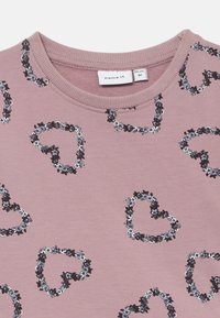 T-shirt de algodão cor-de-rosa com decote redondo, apresentando um padrão repetido de corações feito com acentos florais em preto, branco e azul.