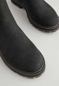 Mustad mustad jalatsid, mis on valmistatud tekstureeritud nahast, ümara varba, tugeva tallaga, millel on sooned, ja tugevdatud servaga.