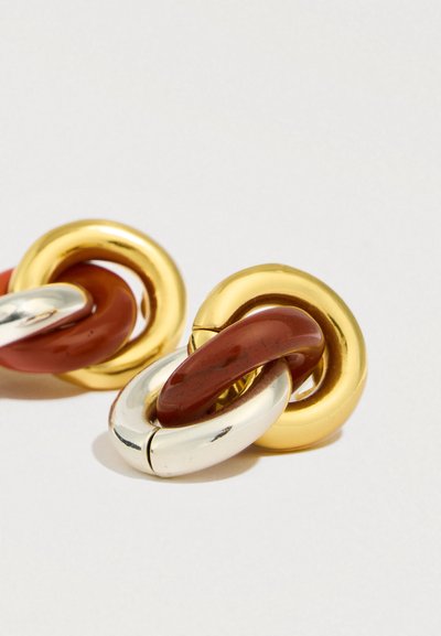 Kultaiset ja hopeiset metalliset korvakorut, joissa on toisiinsa kietoutuvia pyöreitä renkaita, ja kiiltäv�ä punainen korostus. Sileä pinta ja kiillotettu viimeistely.