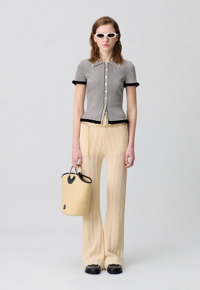 Top de punto a rayas con mangas cortas y ribete negro, pantalones de pierna ancha de canalé beige, y un bolso texturizado beige con acentos negros.