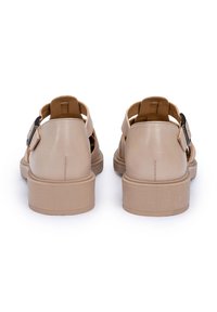 Sandali in pelle beige con fibbia regolabile, design aperto e suola piatta di un marrone chiaro con texture. Presentano dettagli di cucitura.