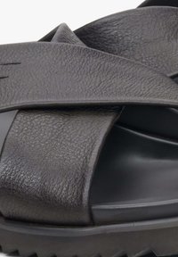 Czarne skórzane klapki z wyraźnym, krzyżowym wzorem paska oraz grubą gumową podeszwą, oferujące nowoczesny, smukły kształt.