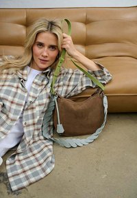 Hnedá semišová kabelka s pleteným svetlomodrým remienkom a zeleným nastaviteľným akcentom. Kabelka má zipsové zapínanie a štruktúrovaný tvar.