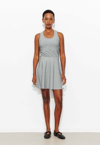 Robe grise sans manches avec un corsage ajusté et une jupe évasée ; fabriquée en tissu doux, avec une texture lisse et un éclat subtil. Chaussures noires à motifs.