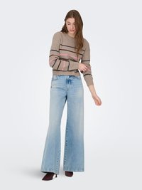 Pull en tricot beige à rayures horizontales roses et marron foncé, associé à un jean large bleu clair et des bottines à talons bordeaux.