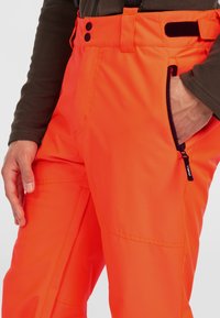 Klarsynta orange vattentäta byxor med texturerad yta, som har en sidoficka med dragkedja, bred midjeband med knappar och kardborre-accenter.