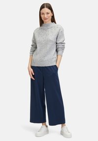 Maglione grigio a maglia con un collo alto e un motivo geometrico testurizzato, abbinato a pantaloni a palazzo blu navy e sneakers bianche.
