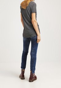 Grå kortärmad t-shirt tillsammans med blå urblekta jeans och vinröda ankelstövlar. T-shirten har en rund halsringning och en avslappnad passform.