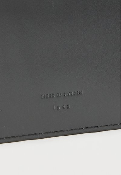 Μαύρη δερμάτινη ετικέτα με ανάγλυφο κείμενο: "TIGER OF SWEDEN" και "1993." Λείο υφή με ελαφριά γυαλάδα, ραμμένες άκρες.