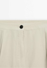 Ceinture de pantalon beige avec des plis et une fermeture à bouton unique noir au centre avant.