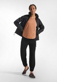 Kevyt musta takki, oranssi lyhythihainen paita, mustat kapealahkeiset housut ja ruskeat nauhakengät. Sulavat tekstuurit, yksinkertainen muotoilu.