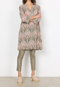 Tunique rose à motif paisley, manches trois-quarts, associée à un pantalon ajusté vert et des chaussures beiges à enfiler.