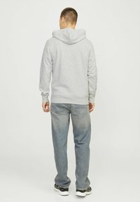 Sudadera gris con una gran capucha, bolsillo canguro, puños y dobladillo acanalados, combinada con jeans de mezclilla azul claro y zapatillas negras.