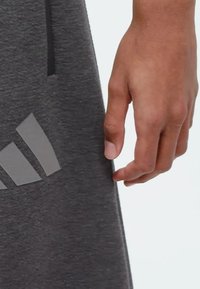 Sivé športové šortky s hladkou textúrou, bočnou vreckom a výrazným šedým logom Adidas na ľavej strane pri leme.