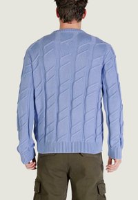 Pull bleu clair en maille avec motif torsadé, col et poignets côtelés, offrant une coupe décontractée et une surface texturée.