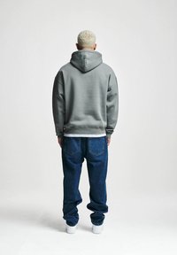 Grå fleece hettegenser med snøring, parret med blå denim jeans og hvite joggesko, sett bakfra. Behagelig antrekk, avslappet passform.