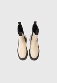 Bottines noires et beiges avec des panneaux élastiques sur les côtés et des languettes, présentées de dessus sur un fond blanc.