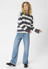 Polo à manches longues avec des rayures horizontales en crème, marron foncé et bleu ; associé à un jean évasé bleu clair et des chaussures noires.